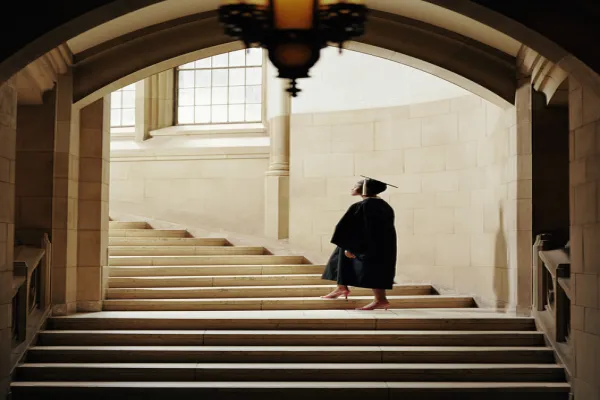 Women wearing graduation cap and gown, ascending staircase, rear view