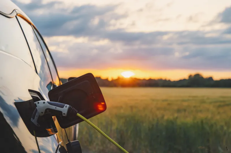 An electric car plugged in against a background of a rural location at sunset
