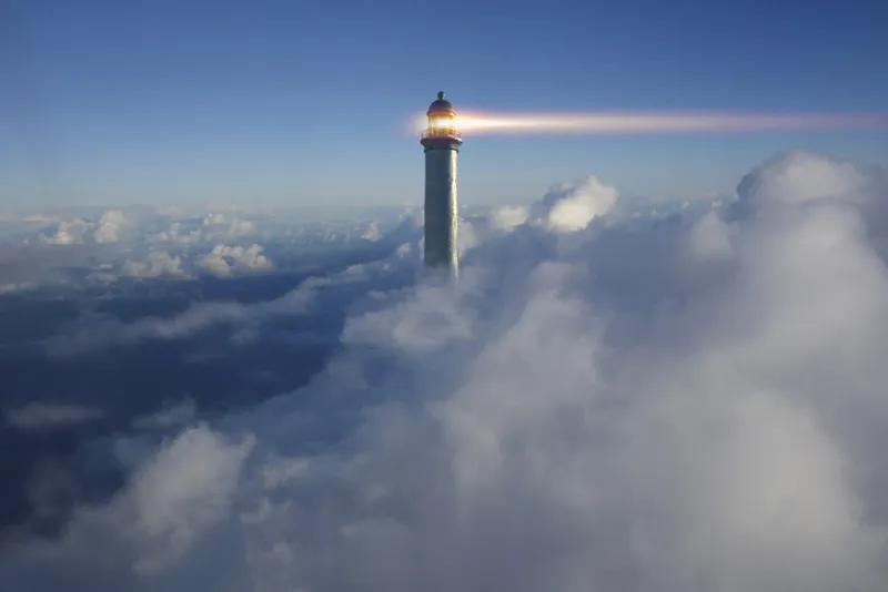 Lighthouse beaming above clouds in blue sky