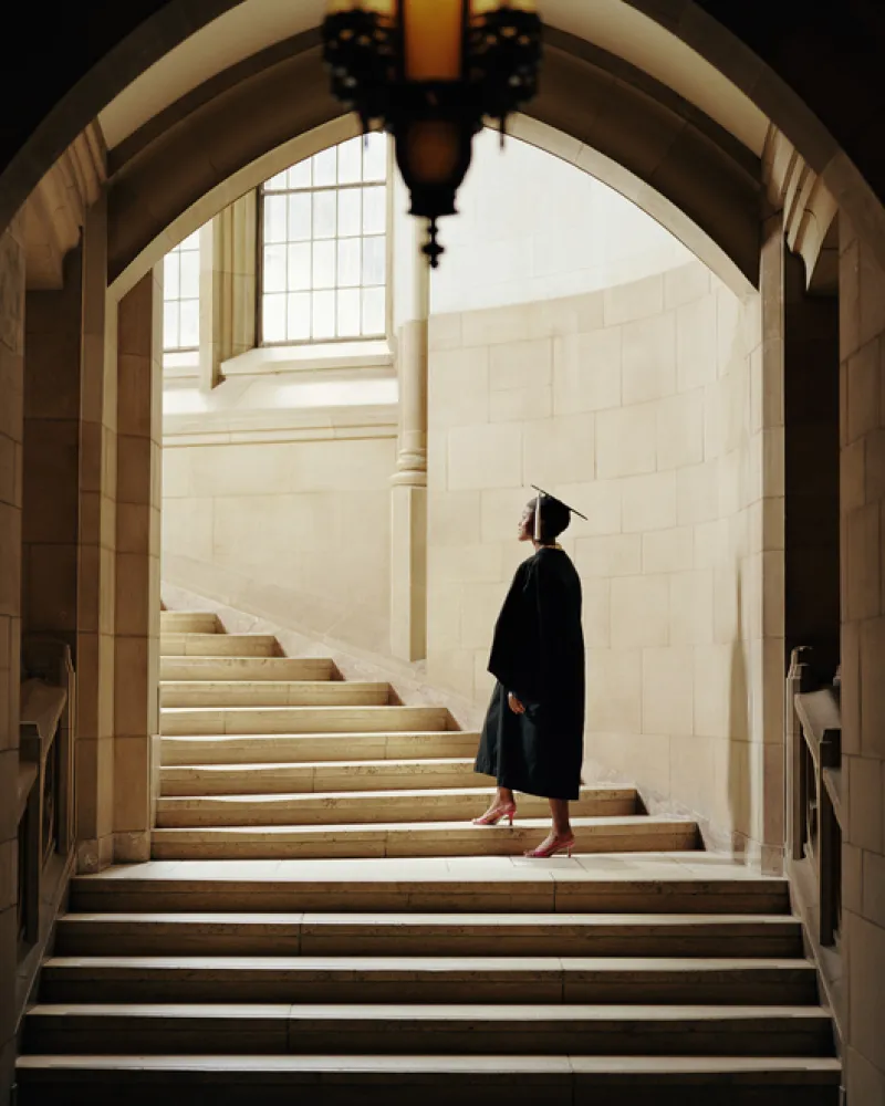 Women wearing graduation cap and gown, ascending staircase, rear view